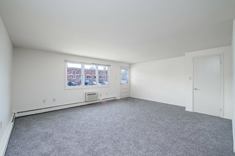 A room with a grey carpet and a window showing a view of buildings outside.