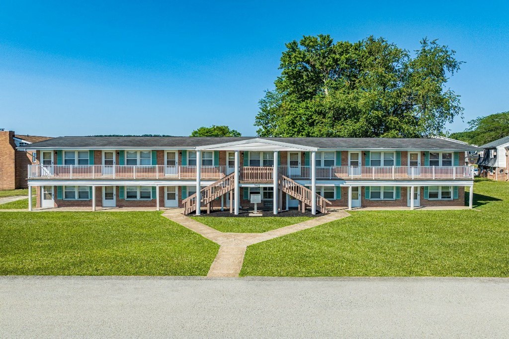 A large building with a grassy area in front and a tree behind it.