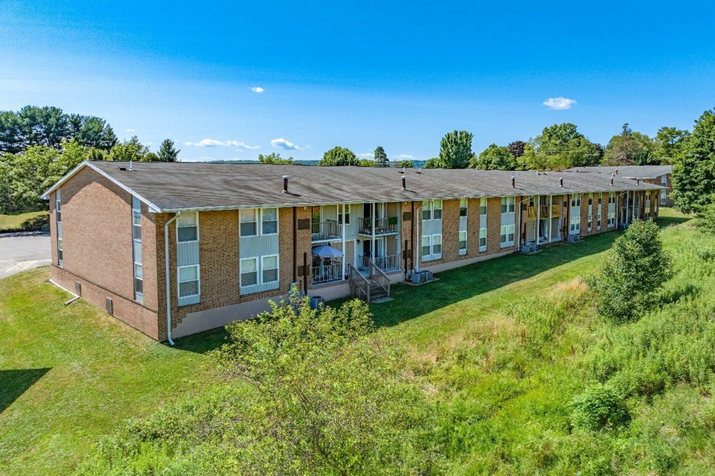 A long building with a brown roof and glass windows sits on a grassy area.