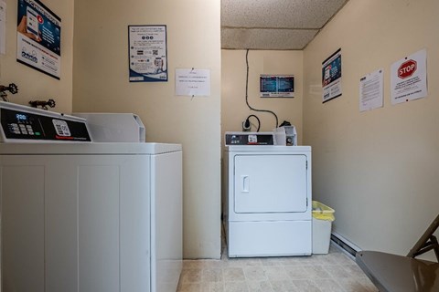A white refrigerator is in a room with a white wall and a white floor.