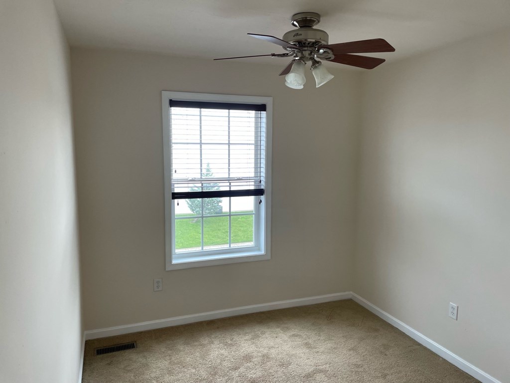 A room with a ceiling fan and a window overlooking a green area.