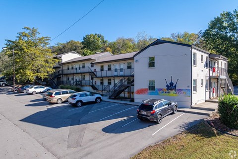 A white building with a mural on the side has cars parked in front.