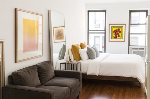 A bedroom with a bed, a couch, and a painting on the wall.