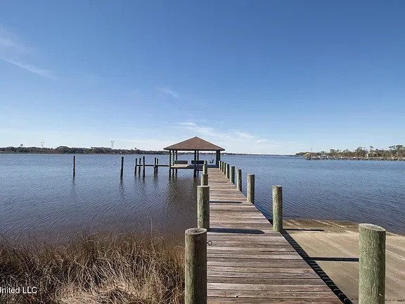 A wooden pier extends into a calm body of water under a clear blue sky.