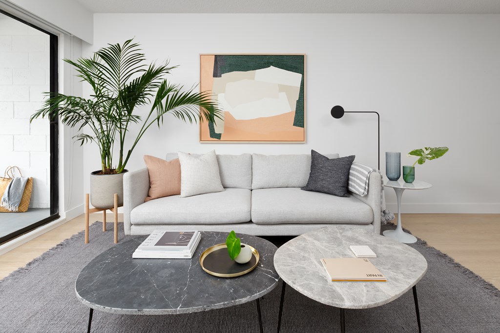A living room with a white couch, a grey coffee table, and a large painting on the wall.