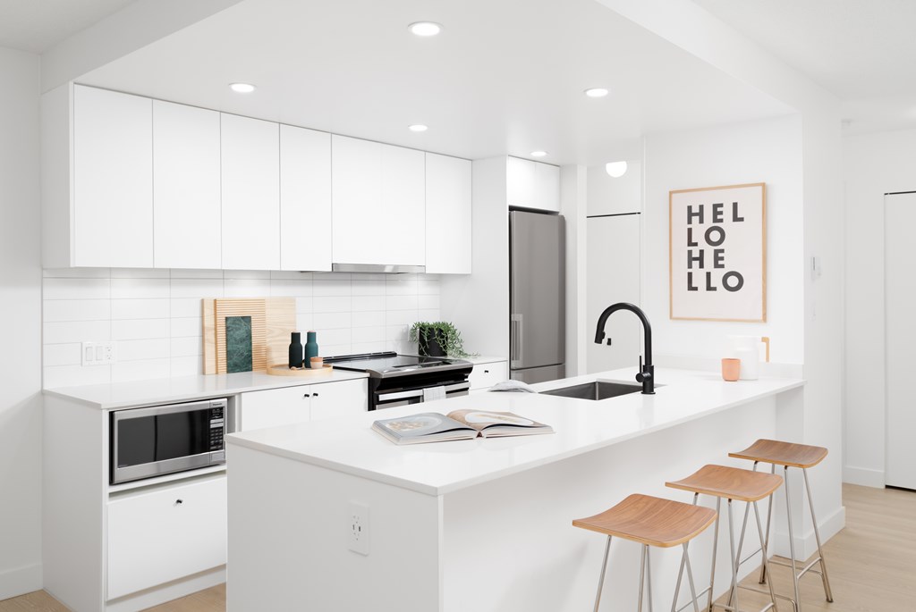 A kitchen with white cabinets and a white countertop with a sink and bar stools.