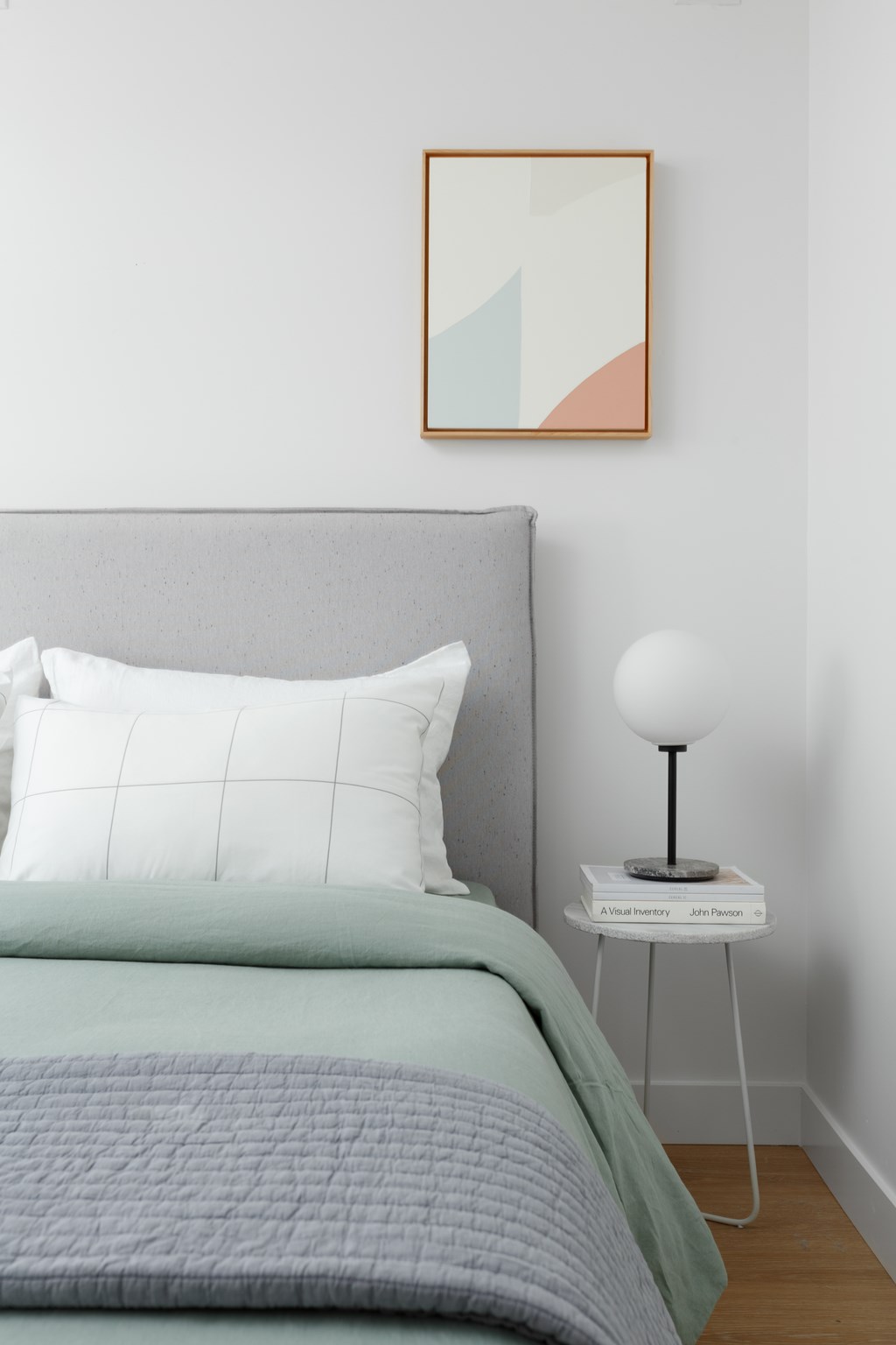 A bed with a grey headboard and a white pillow with a grey blanket on it.