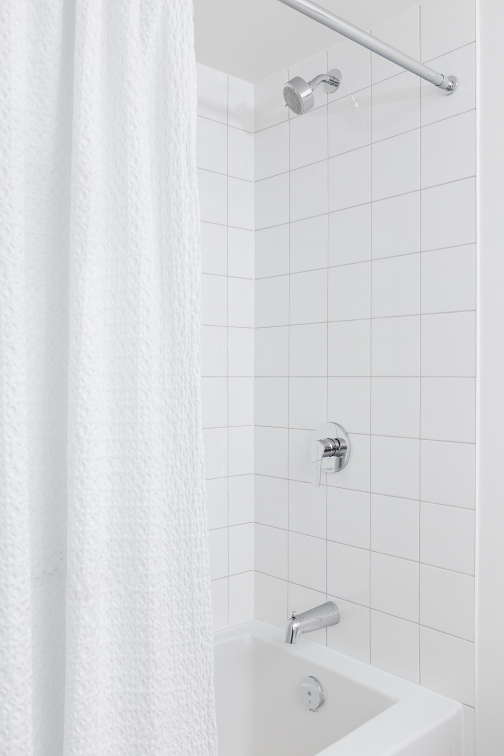 A white shower curtain hangs over a white bathtub.