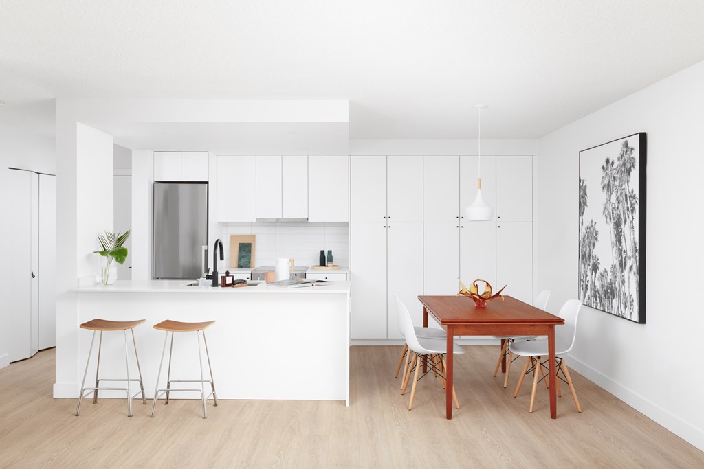 A modern kitchen with a white countertop and a wooden dining table.