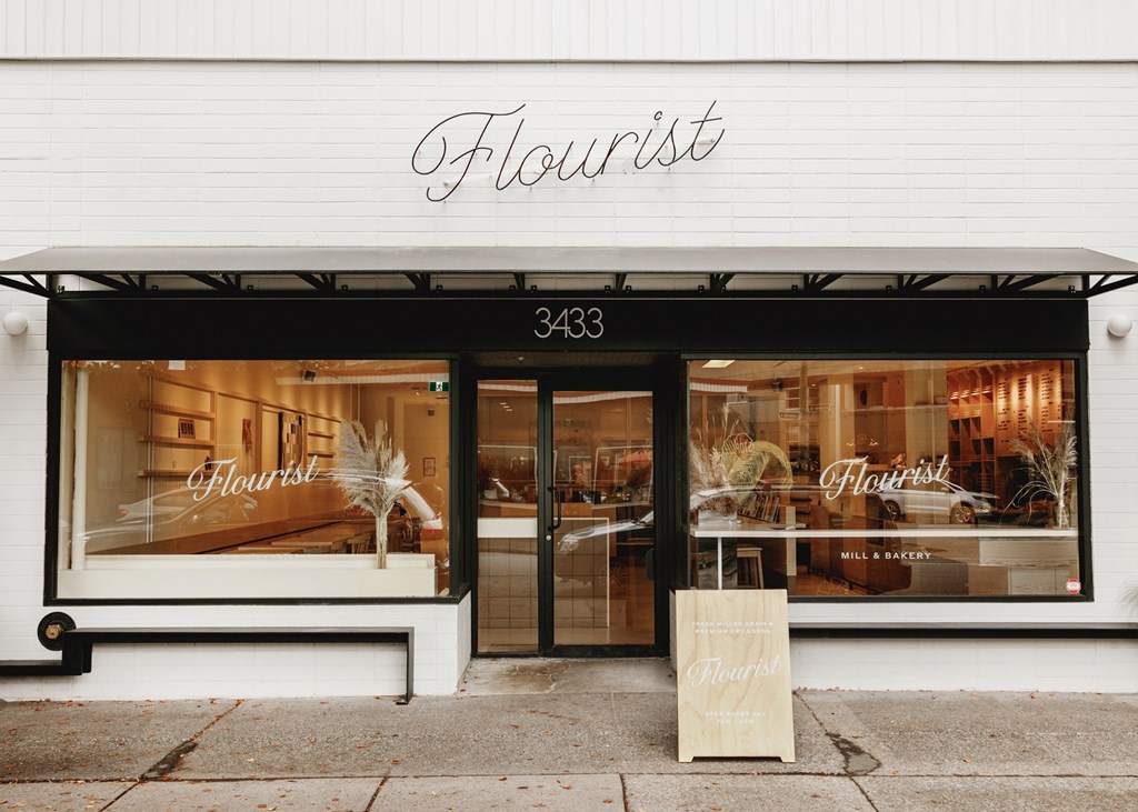 A storefront with a sign that reads "Flourist" and a window display featuring a cake.
