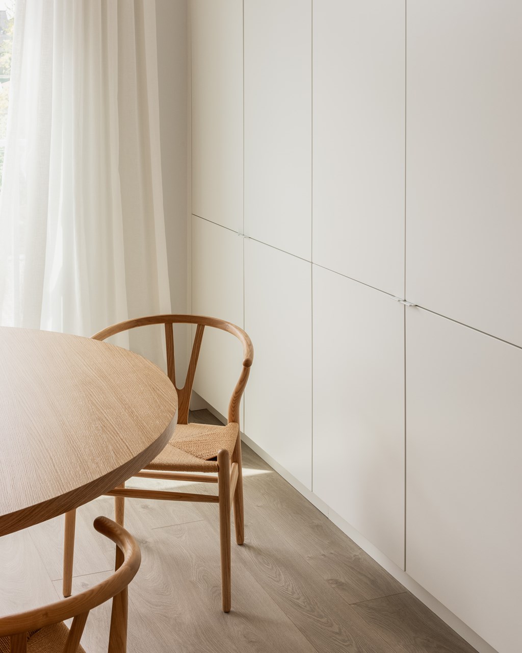 A wooden chair sits next to a table in a room with white walls.
