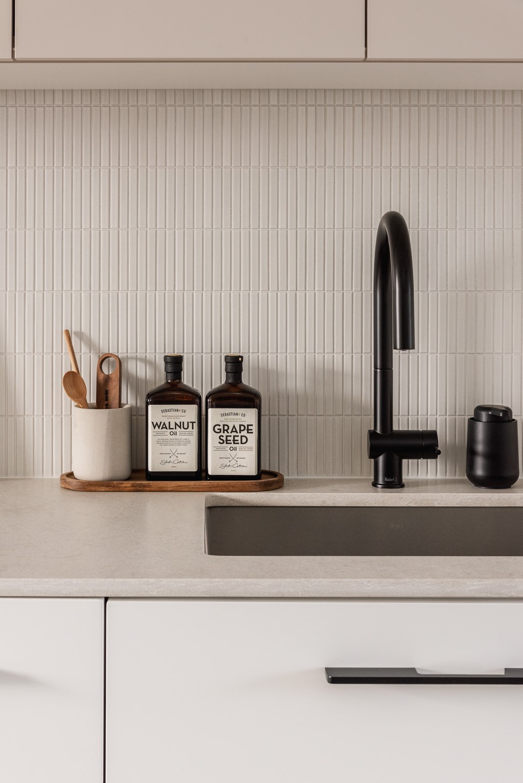 A kitchen counter with a sink, a bottle of grape seed oil, and a bottle of walnut oil.
