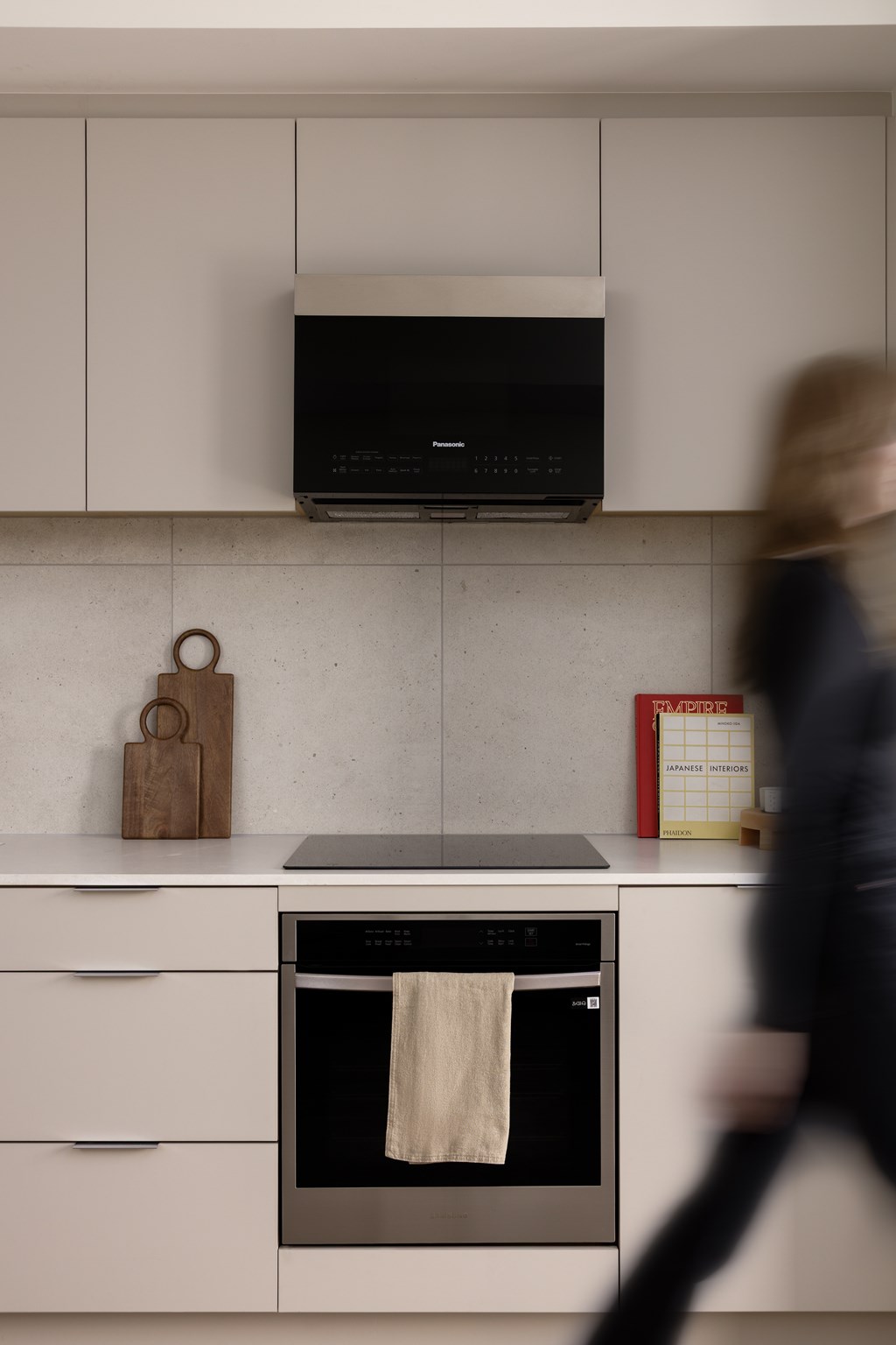 A woman walks past a stove top oven with a towel hanging from it.