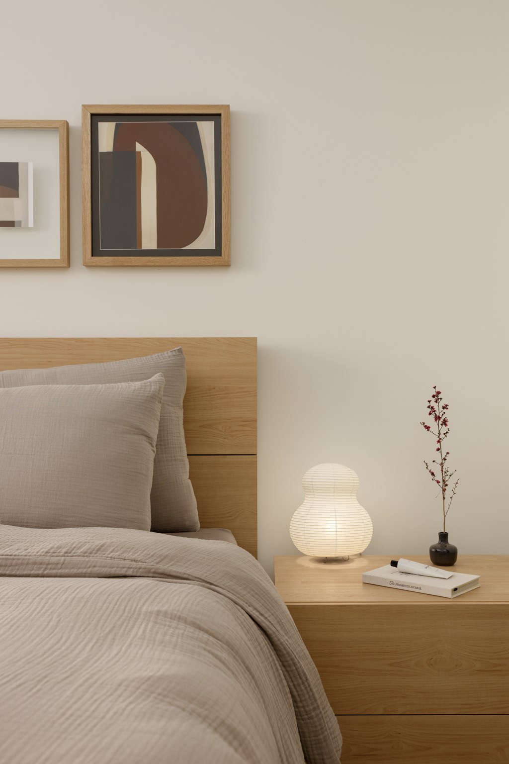 A bed with a grey comforter and a pillow with a lamp and a plant on the nightstand.