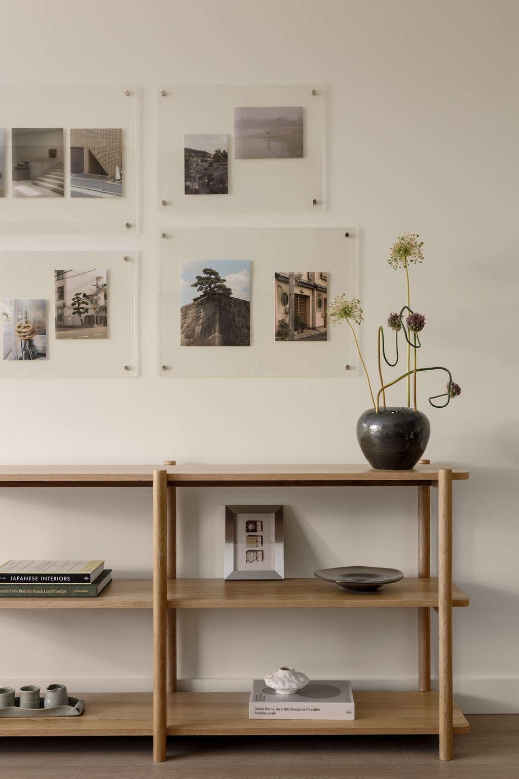 A shelf with a vase on top and pictures on the wall.