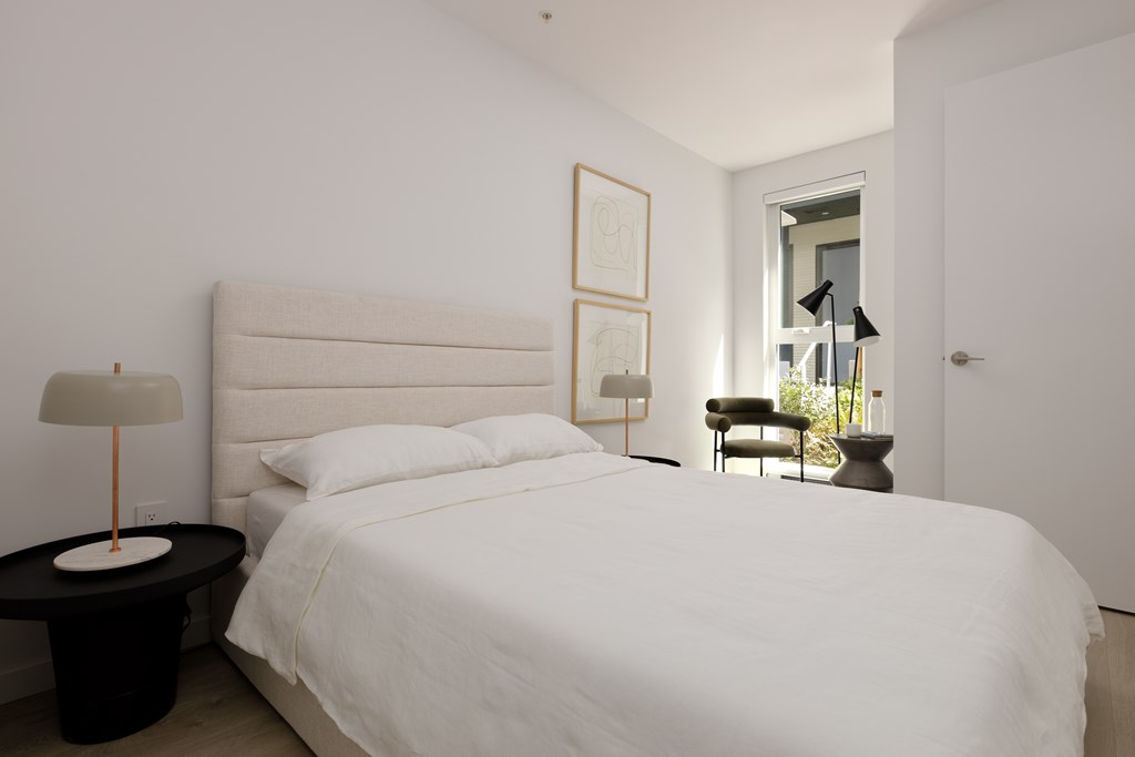 A white bed with a black table and a lamp on it.