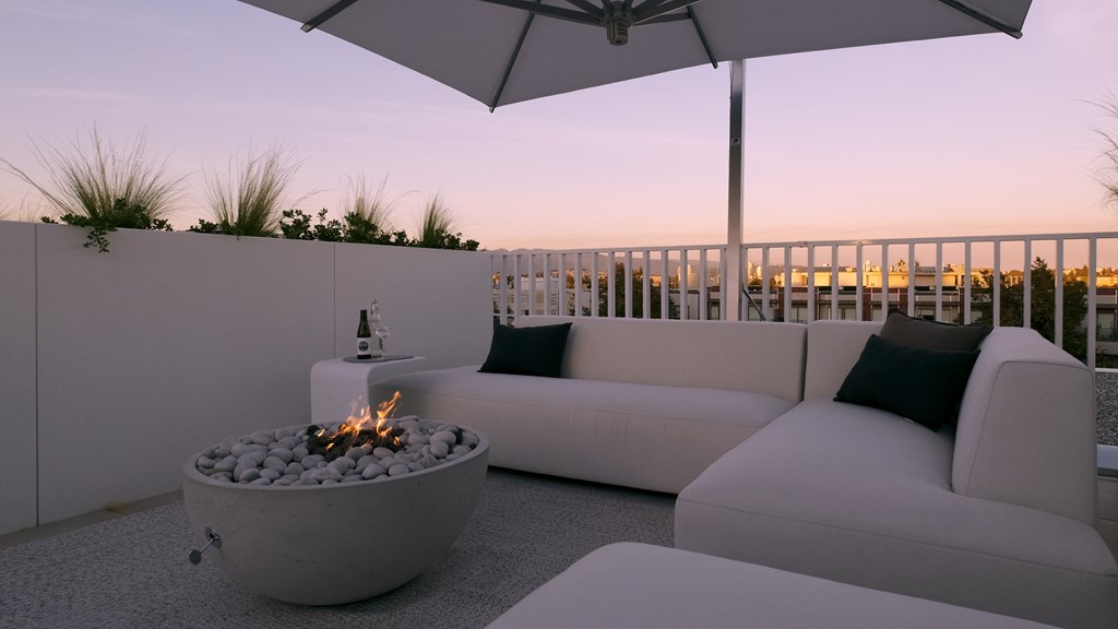 A patio with a fire pit and white furniture.