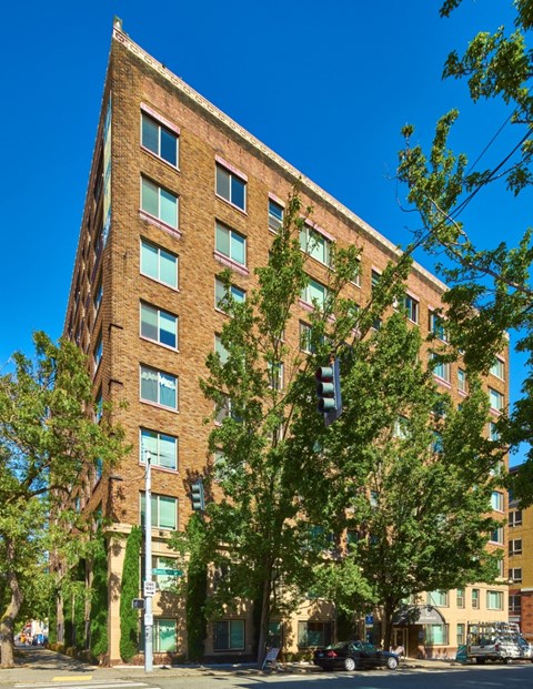 A tall brick building with many windows and trees in front.