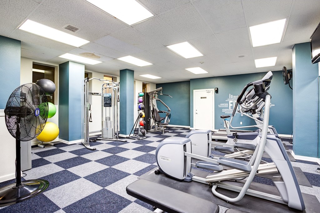 A gym with a fan, weights, and exercise equipment.