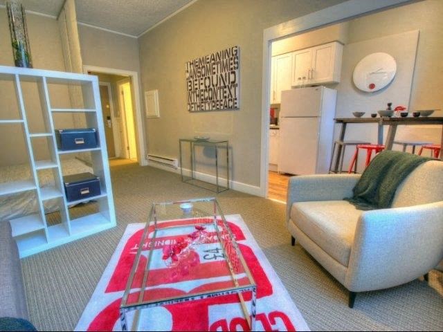 A living room with a chair, rug, and a kitchen in the background.