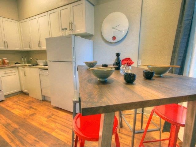 A kitchen with a white refrigerator, white cabinets, wooden table, and red chairs.