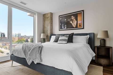 A bedroom with a large bed and a city view through the window.