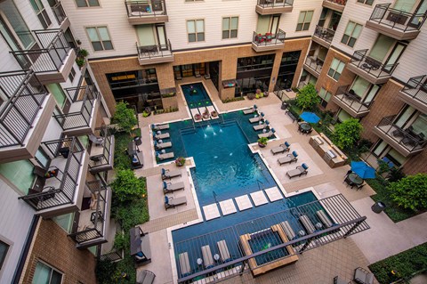A large swimming pool surrounded by lounge chairs and balconies of apartment buildings.