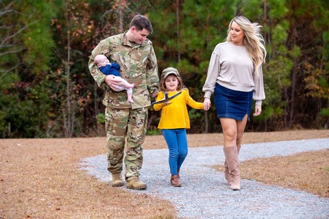 A family of three, including a soldier, are walking together.