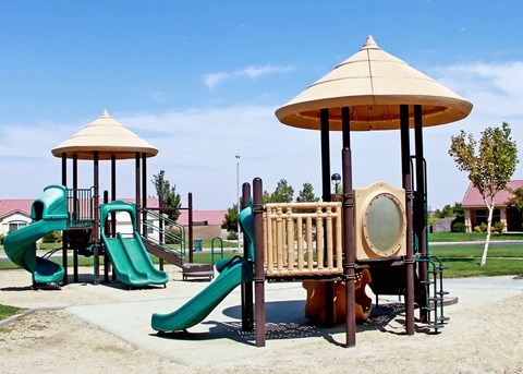 A playground with a green slide and a brown wooden structure.
