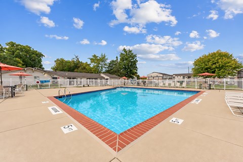A large outdoor swimming pool with a red brick border and a clear blue sky above.