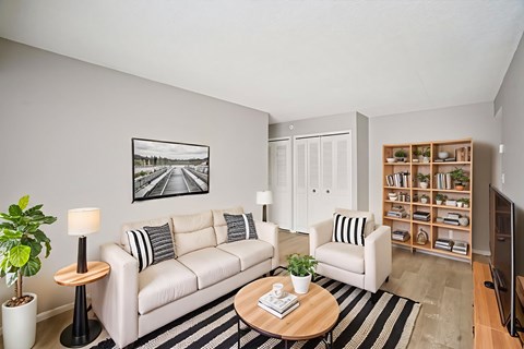 Living room with beige sofa and wood bookshelf at Cambridge on Ford Apartments, Michigan, 48187
