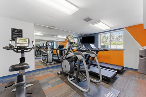 A gym with a row of treadmilers and elliptical machines.