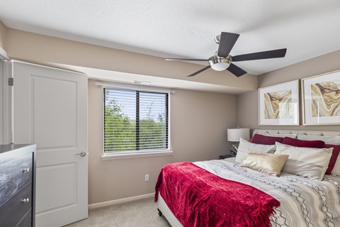 A bedroom with a bed covered in a red blanket and a ceiling fan.