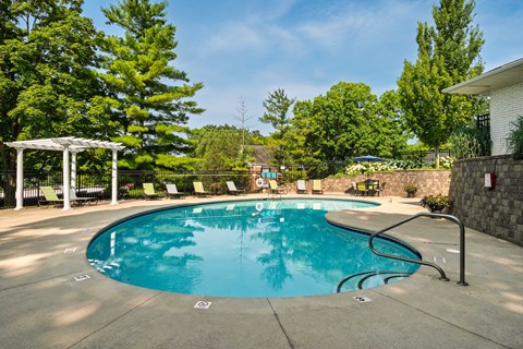 A large outdoor swimming pool surrounded by trees and a white pergola.