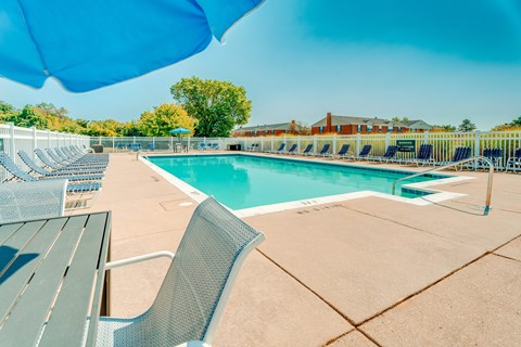 Outdoor swimming pool with lounge chairs and umbrella at Canterbury Square Apartments, Troy, Michigan
