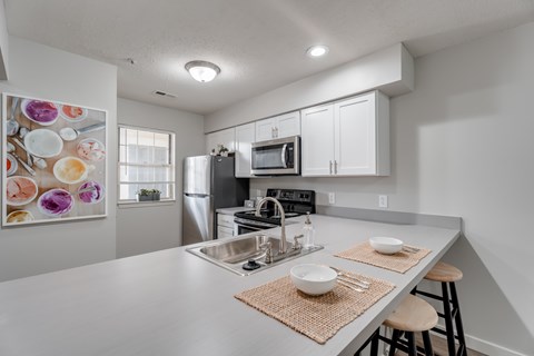 A modern kitchen with a stainless steel refrigerator, microwave, and a sink with a mat on the counter.