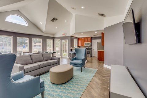 A living room with a grey sofa, a blue armchair, a white chair and a TV mounted on the wall.