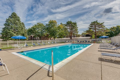 Swimming pool surrounded by lounge chairs and trees at Deerfield Woods Apartments, Michigan