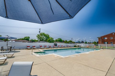 Resort style pool with umbrella shade and deck chairs at Kingsley Apartments, Sterling Heights, MI