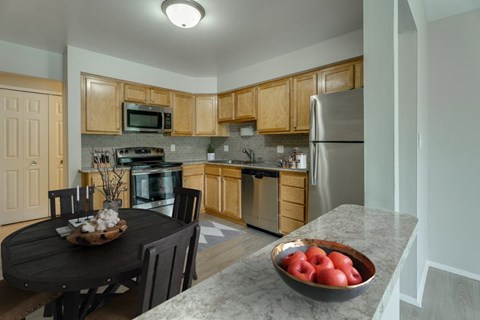 A kitchen with wooden cabinets and a black table with a bowl of apples on it.