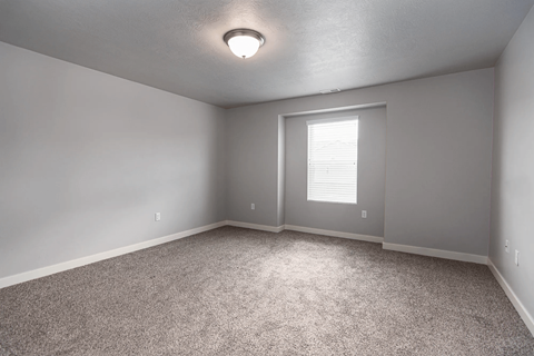 A room with a carpeted floor and a window with blinds.