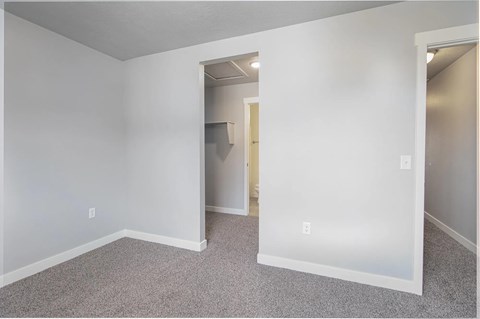 A room with white walls and carpeted floor with a doorway leading to another room.