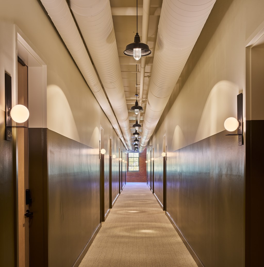 A long hallway with doors on both sides and lights hanging from the ceiling.