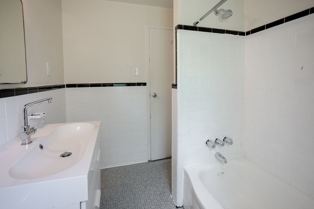 A white bathroom with a sink, mirror, and bathtub.