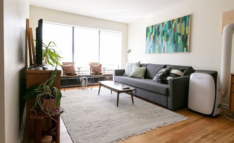A living room with a grey couch and a large painting on the wall.