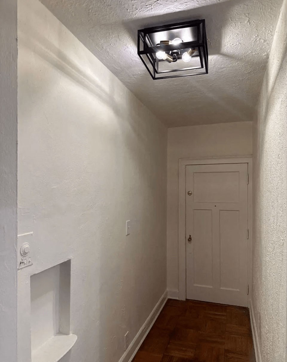 A white hallway with a light on the ceiling and a door at the end.