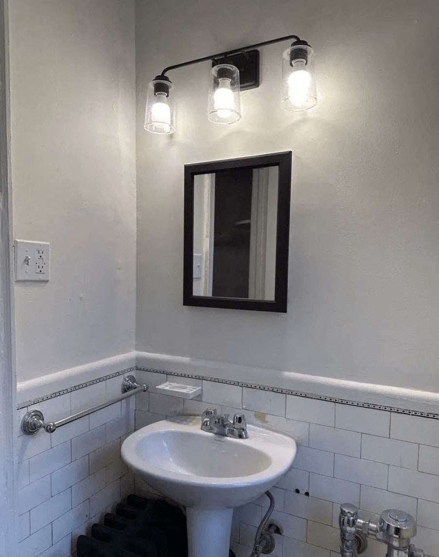 A white sink in a bathroom with a mirror and lights above it.
