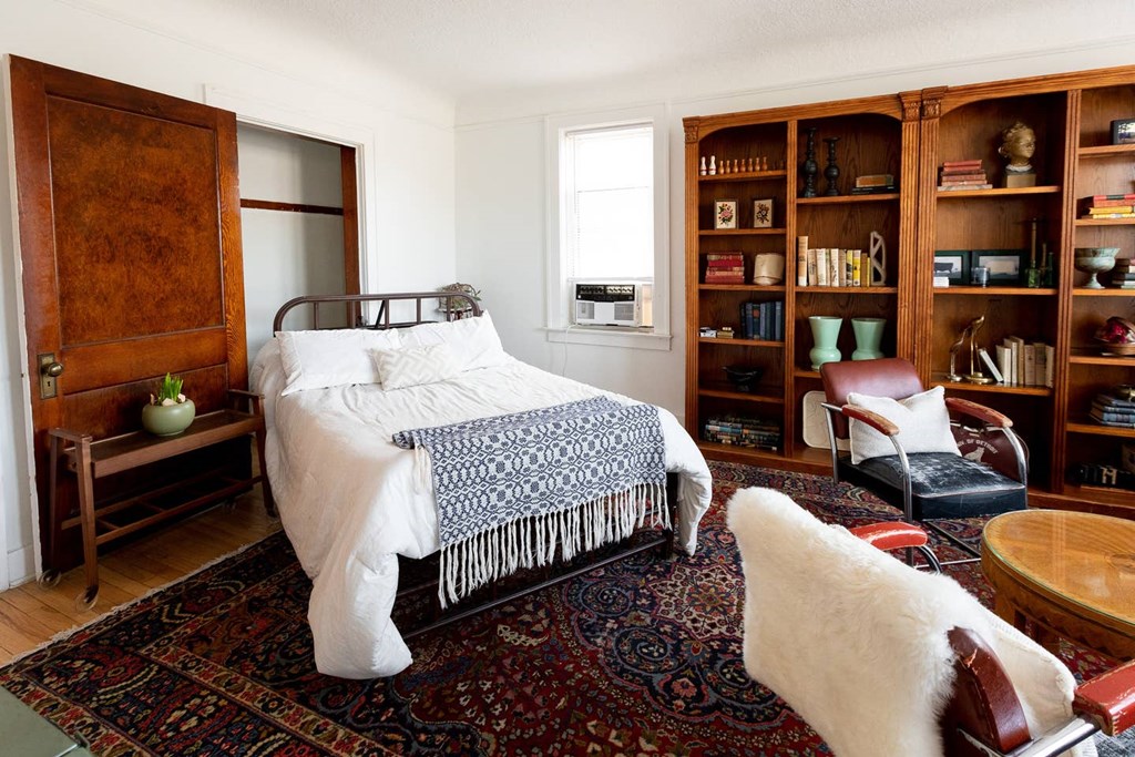 A bedroom with a bed, chair, and bookshelf.