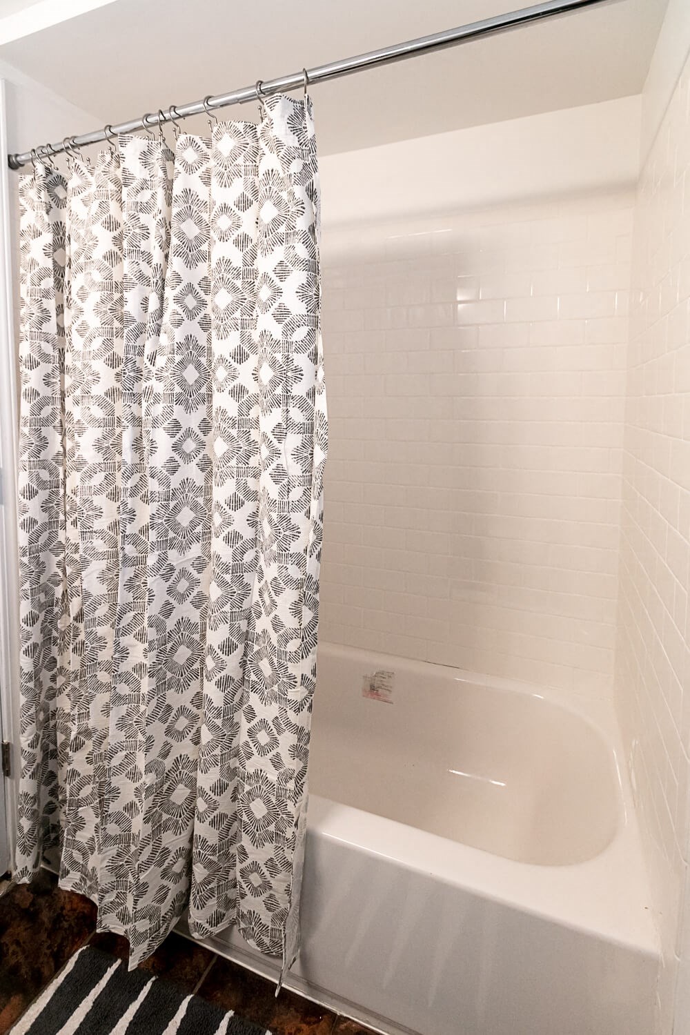 A shower curtain with a black and white pattern hangs over a white bathtub.