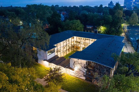 A modern building with a dark roof and lit windows is surrounded by trees.